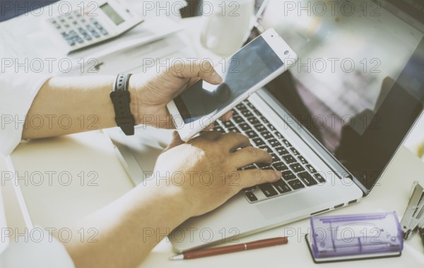 Businessman hand using smart phone and keying the data to laptop, mobile payments online shopping.Seleted focus