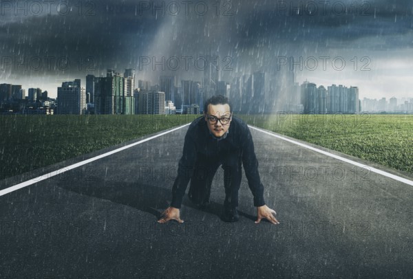 Young businessman starting position to his career with city skyline background, raining day . Determined to start concept