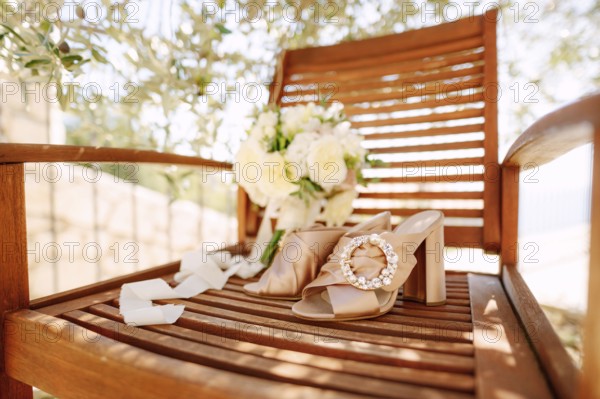 Close-up of a wooden chair with a round buckle clog and a bouquet of flowers under an olive tree.