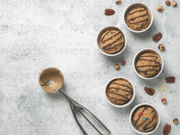 Safe-to-eat raw monster cookie dough in small portion bowl, ice cream scoop and nuts on gray cement background. Ideas and recipes for kids and toddlers meal. Top view or flat-lay. Copy space for text