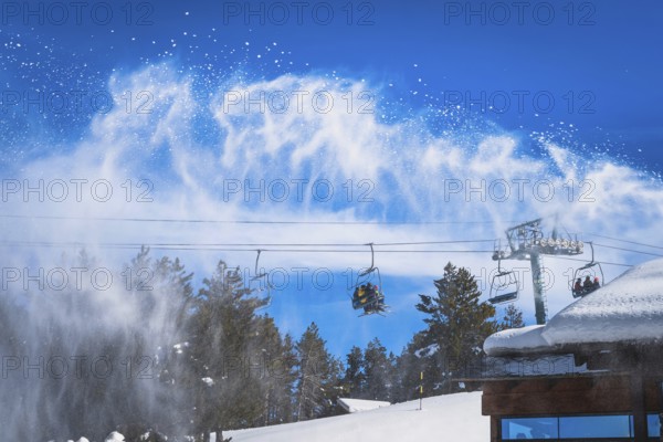 Snow cannon spreading fresh snow powder on a ski slope. Skiers riding up on chair lift. Winter ski holidays in El Tarter, Andorra, Pyrenees Mountains, Europe