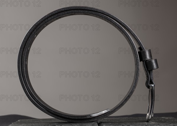 Leather belt twisted into a circle on a grey background