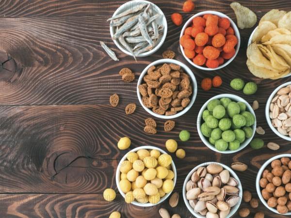 Assortment of different snack for beer, wine, party. Peanuts in coconut glaze, green vasabi, red spicy chilli, yellow cheese glaze, chips, pistachio, crackers, fish on brown wooden table. Copy space