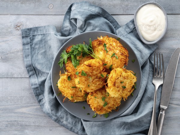 Close up view of potato pancakes. Potatoes pancakes latkes, flapjacks, hash brown or potato vada on gray plate over gray wooden table, with fresh parsley and sour cream. Copy space for text
