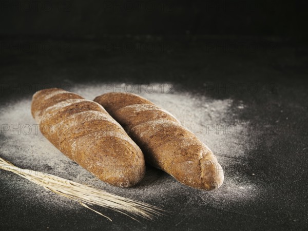 Two whole homemade rye loaf bread with buckwheat flour on black textured background. Copy space. Low key