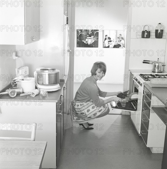 In the kitchen in the 1960s. A young woman in the kitchen taking out the ready baked breads from the oven. The food procossor in it's typical 1960s look is seen on the kitchen counter. Sweden 1963. ref BV79-9