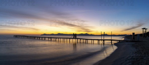 Peaceful sunrise seascape with an old wooden dock leading out into the calm ocean waters of Alcudia Bay