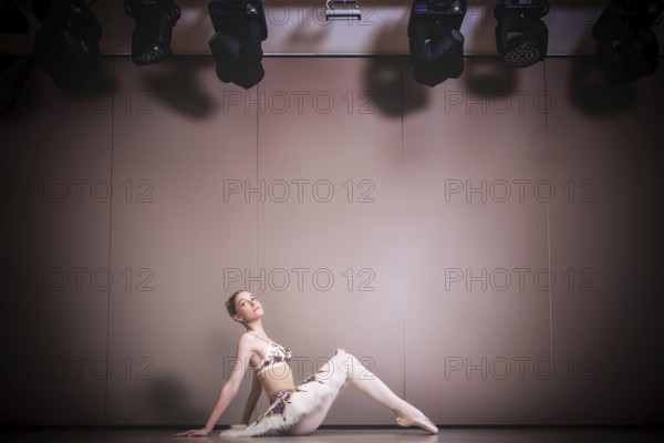 Young beautiful graceful caucasian ballerina practice ballet positions in tutu skirt. Classical Ballet dancer sitting on the floor in the studio