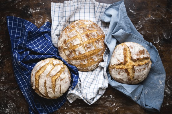 Above view with three homemade sourdough loaves of bread on towels. Freshly baked and delicious white bread