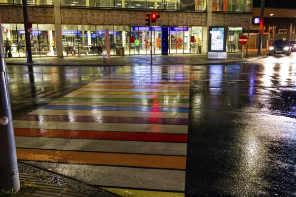 Rainy asphalt, zebra crossing in rainbow colours leads to the station, night shotLeoben, Styria, Austria, Europe