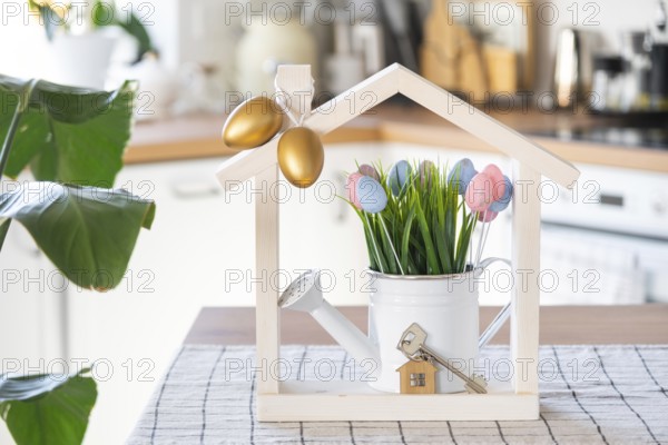 Key and tiny house of cozy home with Easter decor with color eggs on table of kitchen. Building, design, project, moving to new house, mortgage, insurance, rent and purchase real estate