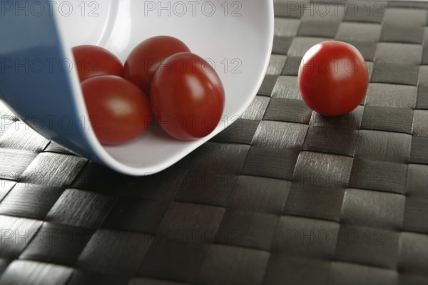 Group of cherry tomatoes falling from blue bowl over brown tablacloth