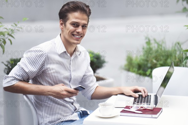Smart attitude. Positive handsome man using a laptop and sitting in the cafe while surfing the internet