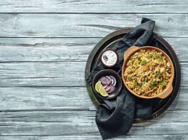 Pakistani food - biryani rice with chicken and raita yoghurt dip. Delicious hyberabadi chicken biryani over tray on gray wooden background. Top view or flat lay. Copy space for text or design