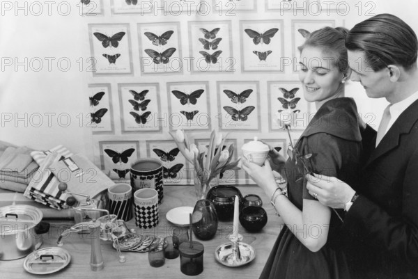 In the 1950s. A young with the typical 1950s designed objects, household appliencies and details on a table in front of them. He is giving her a rose. Sweden 1958