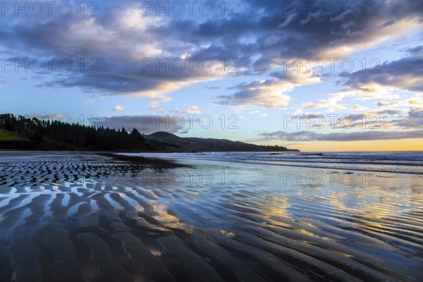 Strips of sand and water left by the ocean tide. Sunrise over the ocean. New Zealand, Pacific Coast. Low tide. The concept of artistic photography. Artistic postal and greeting card
