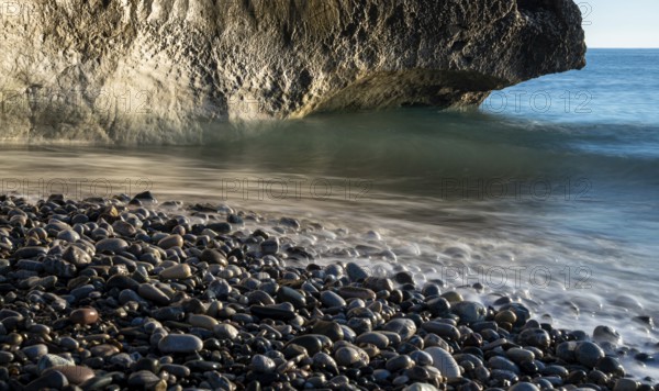 Low angle view of seascape with windy waves splashing on the rock and the sea pebbles. Rock of Aphrodite in Paphos, Cyprus, Europe