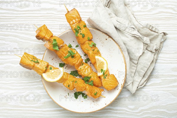 Grilled barbecue salmon skewers seasoned with green parsley and lemon on ceramic plate on white wooden rustic table background top view, healthy eating, food photography, food photography
