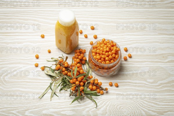Sea buckthorn healthy drink in bottle, ripe berries in glass jar and branches with leaves top view on white wooden rustic background, great for skin, heart, vessels and immune system, food photography, food photography