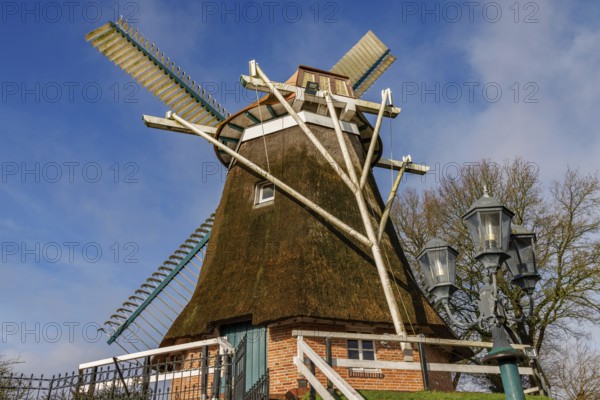 Traditional windmill next to antique looking lanterns against a blue sky, burlage, east frisia, germany