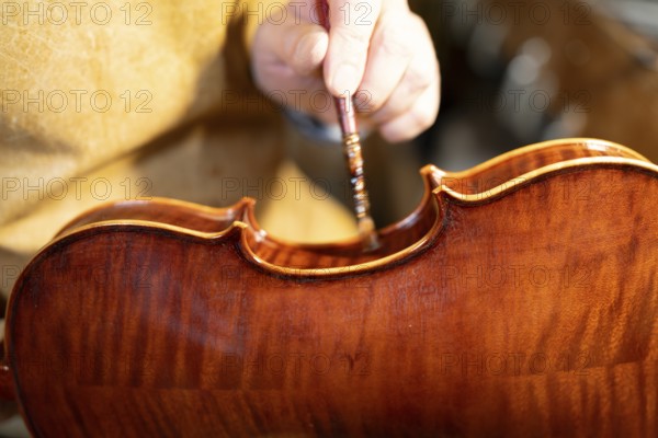 Luthier carefully varnishing a violin with a brush, showcasing the craftsmanship and meticulous process involved in creating stringed instruments