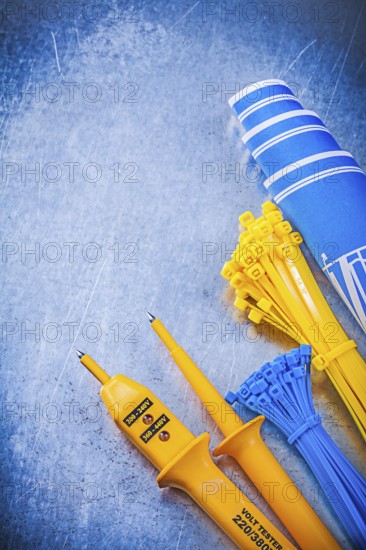 Yellow electrical tester self-locking cable ties blue construction plans on metallic background electricity concept