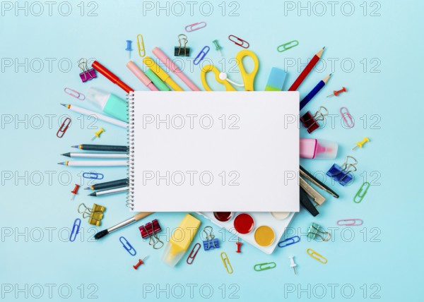 Notebook with stationary objects on blue background. Empty white paper sheet of notepad or sketchbook over shool supplies, isolated on blue. Copy space for text or design. Top view, flat lay