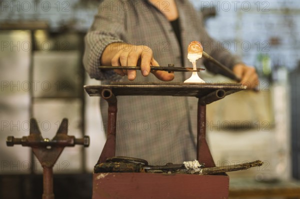 The worker makes a glass ornament in a glass smelter