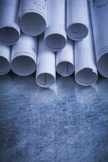 Pile of rolled engineering drawings on scratched silver-metal background building and architecture concept