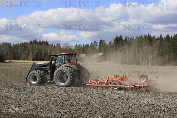 SALO, FINLAND, MAY 7, 2017: Farmer cultivates field with red Valtra tractor and Potila seedbed cultivator on a beautiful day of spring