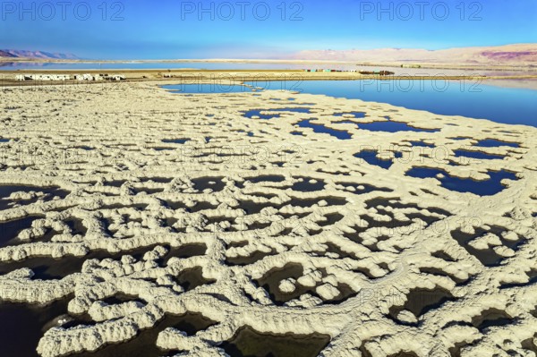 The blue water is surrounded by pink mountains. The picturesque Dead Sea is covered with patterns of salt. Sunny winter day. The picture was taken by a drone from a aerial view. Israel