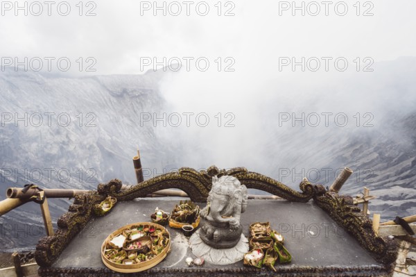 Traditional offerings and a statue on an altar with a misty volcano background, Bromo volcano, Sri Lanka, Asia
