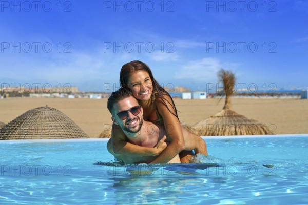 Tourist couple piggyback in infinity pool on a beach resort in summer vacation