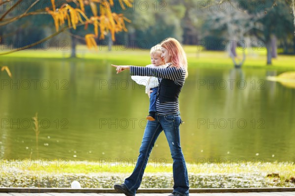 Kid girl and mother walking in the park lake pointing finger