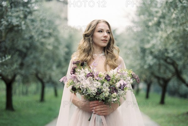Bride with a bouquet of flowers in an olive grove.