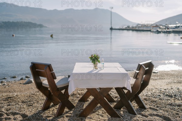Laid table for two with chairs stands on a sandy beach by the sea.