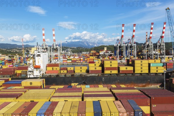 High angle view of stacked rectangular metal box shipping containers on dock waiting to be loaded onto MSC Renaissance III cargo vessel in La Spezia cargo Port, Italy, Europe