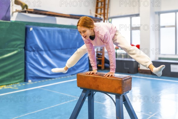 Female student performing gymnastic exercises on pommel horse during physical education class in school gymnasium