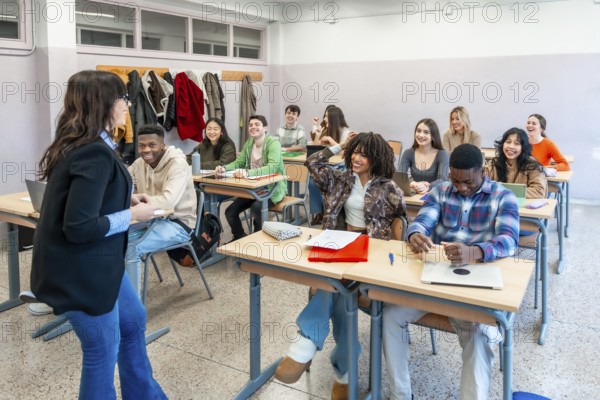 Multi ethnic university students attending a lesson with their professor, participating actively and enjoying learning in a modern classroom