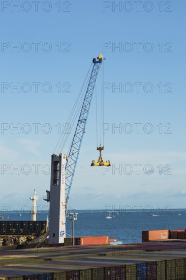 Gotwald crane with lifting attachment and stacked rectangular metal box shipping conatiners on dock in La Spezia cargo Port, Italy, Europe
