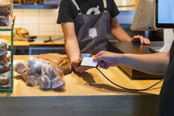 Customer in the bakery shop buying an artisan bread from the baker in the workshop, paying with the card