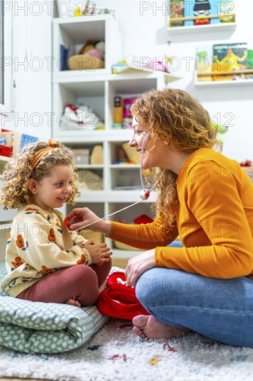 Vertical photo of a caucasian mother listening the beat of daughter heart with fake stethoscope playing nurses and doctors at home