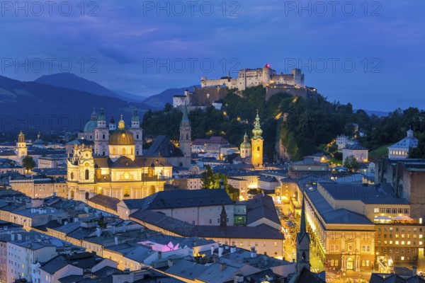 The city of Salzburg glows at dusk, dominated by the Hohensalzburg Fortress and the Alps, Salzburg, Salzburger Land, Austria, Europe