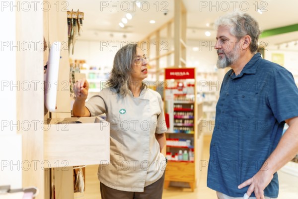 Female adult pharmacist attending a male mature client looking for medicines on computer
