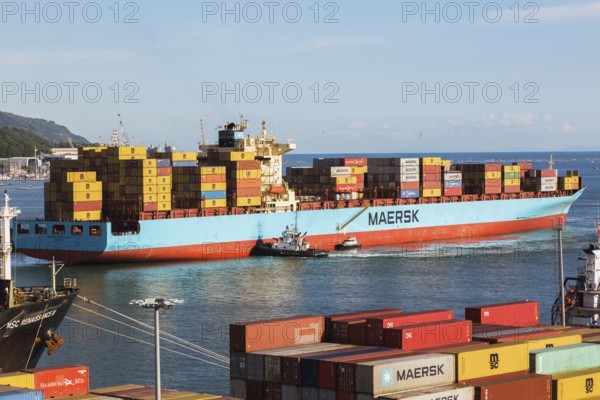 Maersk Serangoon cargo ship loaded with metal box shipping containers being guided by pilot boats into La Spezia cargo Port, Italy, Europe