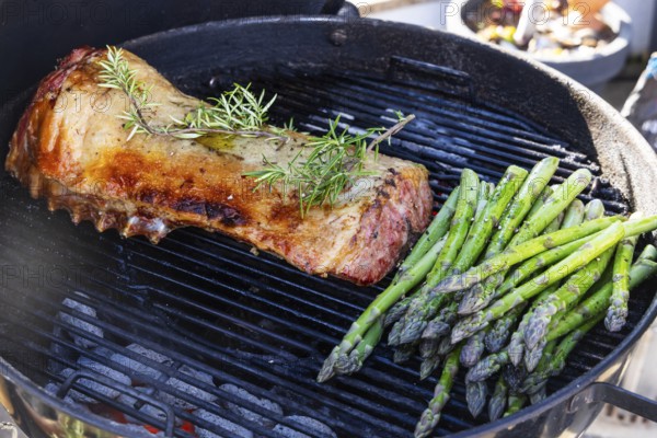 Barbecue with Easter roast. Rack of lamb and green asparagus grilled on an outdoor kettle barbecue. Meat and vegetarian vegetables. Baden-Württemberg, Germany, Europe