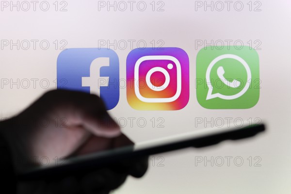 In this photo illustration the Facebook, Instagram and WhatsApp logo app seen in the background of a silhouette hand holding a smartphone