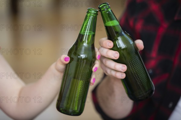A close-up on the hands of two people. Each of them is holding a green bottle without a label. The boy and girl are giving a toast. Blurred background