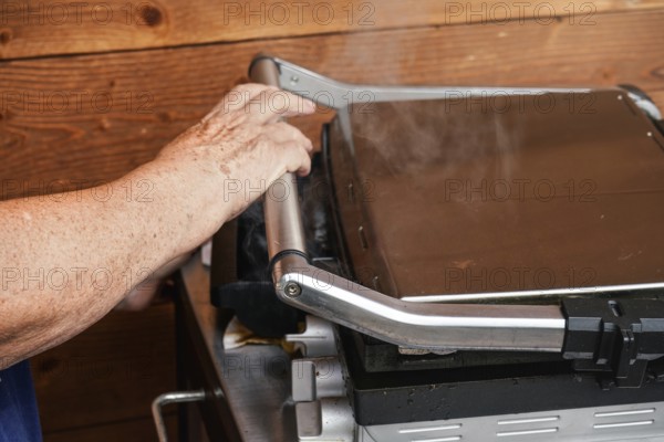 Senior hand closing metal electric grill, smoke coming up from grilled food inside, Pribylina, Slovakia, Europe