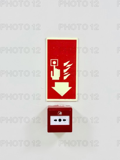 A red fire alarm button with an instructional sign above it on a white wall